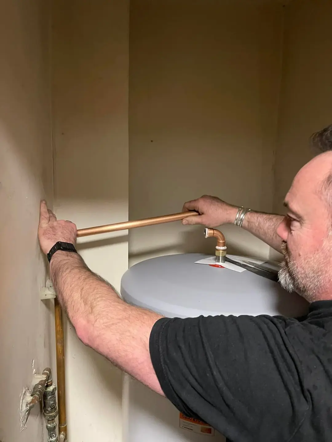 Plumber measuring copper pipe above a hot water cylinder