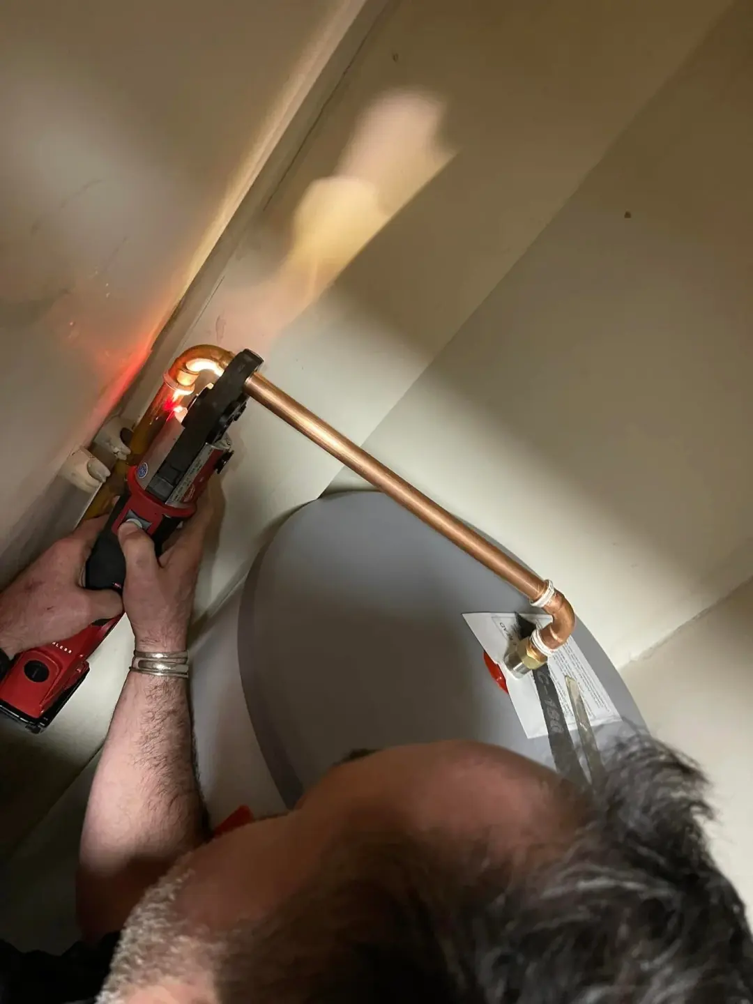 Plumber press-fitting copper pipework on a hot water cylinder