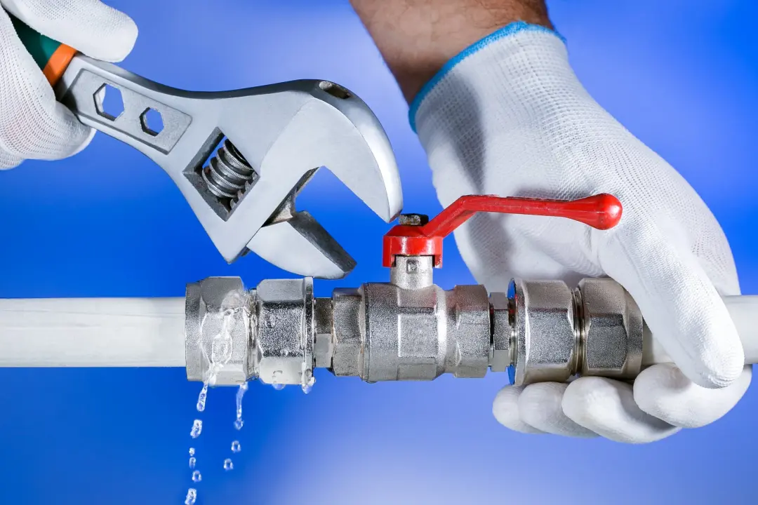 Plumber tightening a leaking pipe valve with a wrench