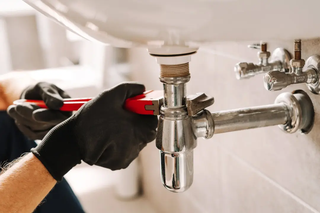 Plumber tightening a basin waste joint with a wrench