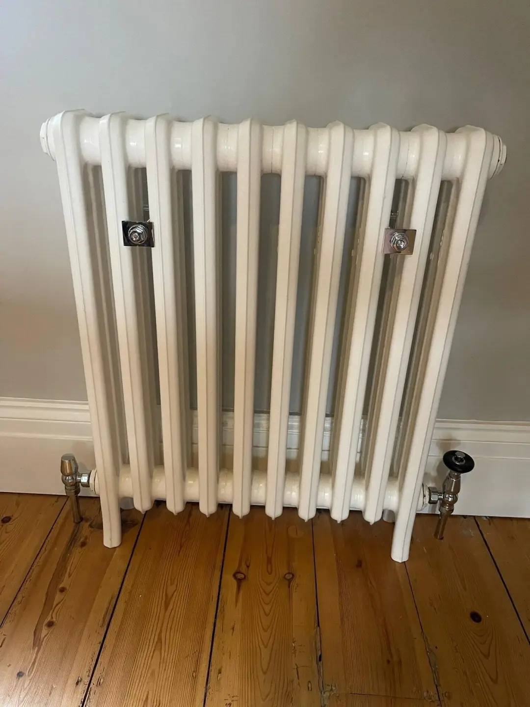 White column radiator with valves on a wooden floor